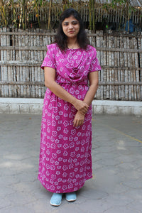 Woman wearing a pink floral dress standing in front of a wooden fence.