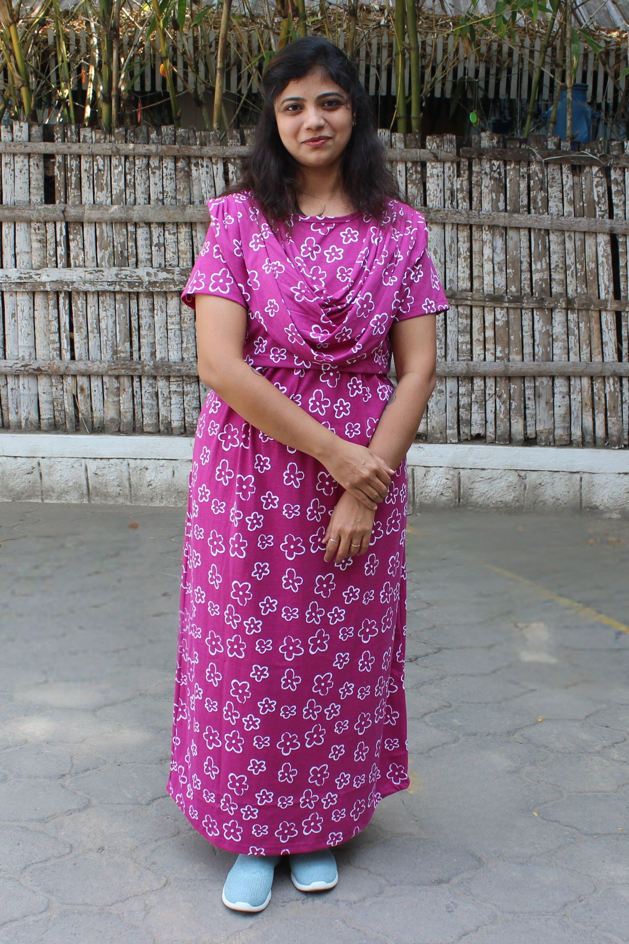 Woman wearing a pink floral dress standing in front of a wooden fence.