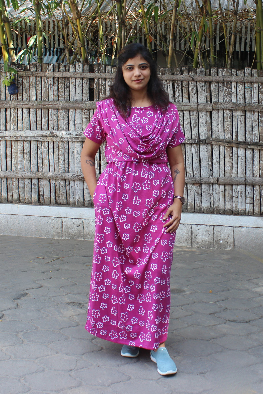 Woman wearing a pink floral dress standing in front of a wooden fence.