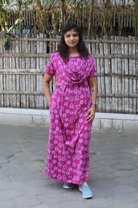Woman wearing a pink floral dress standing in front of a wooden fence.