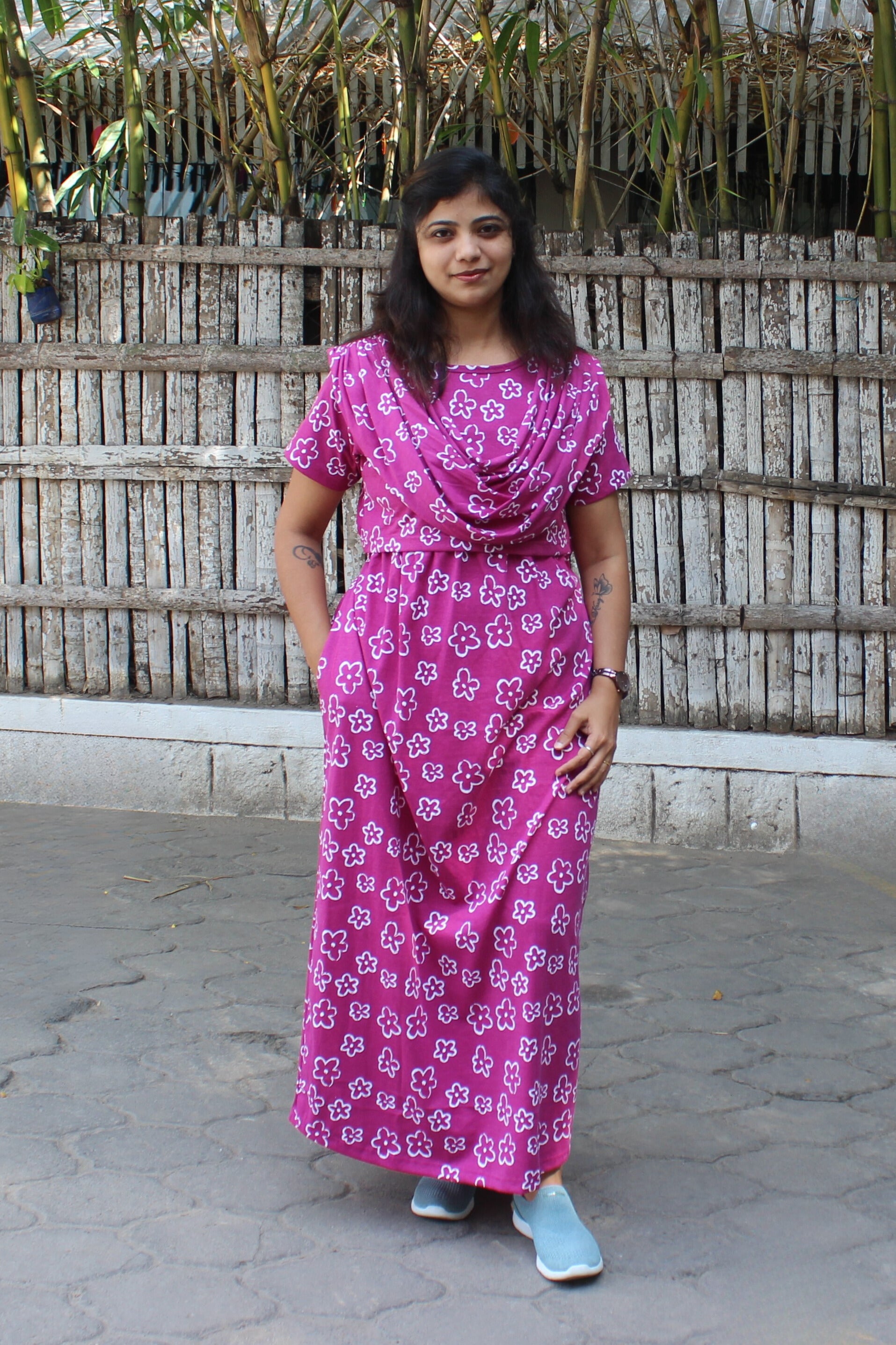 Woman wearing a pink floral dress standing in front of a wooden fence.